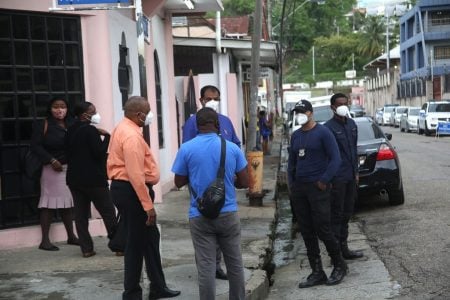 Employees and police officers stand outside the Riverside Plaza in Port-of-Spain.