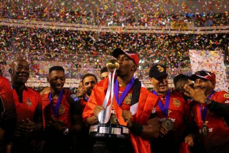 Trinbago Knight Riders captain Dwayne Bravo, centre, kisses the 2018 CPL trophy as Prime Minister Dr Keith Rowley,left, spinner Khary Pierre, second left, manager Colin Borde, second right, and other team officials look on. PHOTO Courtesy CPL
