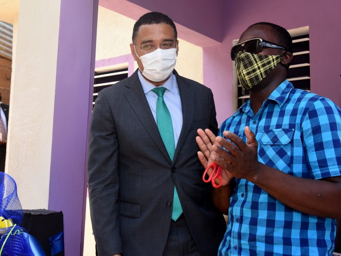 Prime Minister Andrew Holness looks on as Kemoy Thomas applauds after cutting the ribbon to mark the opening of his house delivered under the HOPE programme - Kenyon Hemans