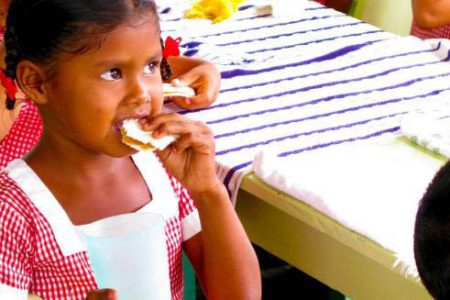 A hinterland nursery school child snacking on a peanut butter and cassava bread sandwich.