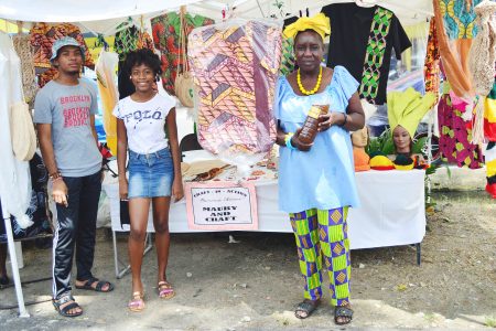 Roxanne Adams (at right), displaying her African wear and mauby along the Main Street Avenue on Wednesday. She is one of several vendors who were showcasing colourful African wear and craft in the avenue this week and among those affected by the shelving of the annual festivities in the National Park this year due to COVID-19.  