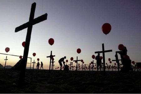 People are seen silhouetted among crosses and balloons placed by members of the NGO Rio de Paz in tribute to the one hundred thousand mortal victims of the coronavirus disease (COVID-19) in the country, at Copacabana beach in Rio de Janeiro, Brazil August 8, 2020. REUTERS/Ricardo Moraes