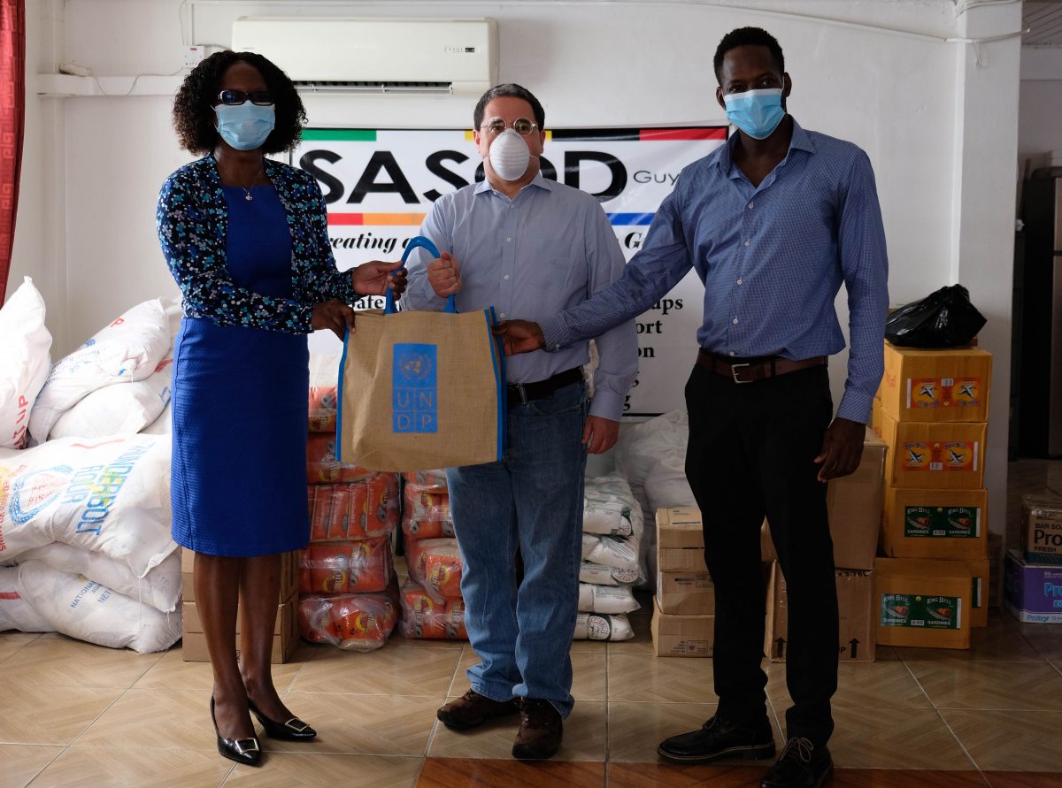 Jairo Valverde (centre), UNDP’s Resident Representative, hands over food items to Dr. Rhonda Moore (left) , Director of the National AIDS Programme Secretariat and  Joel Simpson, Managing Director of SASOD. (UNDP photo)