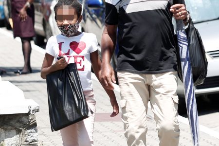 A child and man wearing masks to help prevent the spread of COVID-19 walk along Independence Square, Port-of-Spain, yesterday.