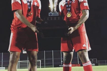 Shaquille Agard (right) of Masters FA displaying the League1 championship trophy alongside a teammate.