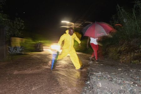 Residents of Nine Miles, Bull Bay walk along Weise Road where the adjacent Chalky River overflowed its banks on Sunday.