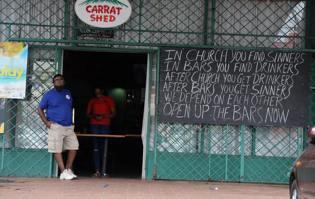 A man stands next to a sign calling for bars to be opened now outside Carrat Shed bar in Marabella on Thursday.