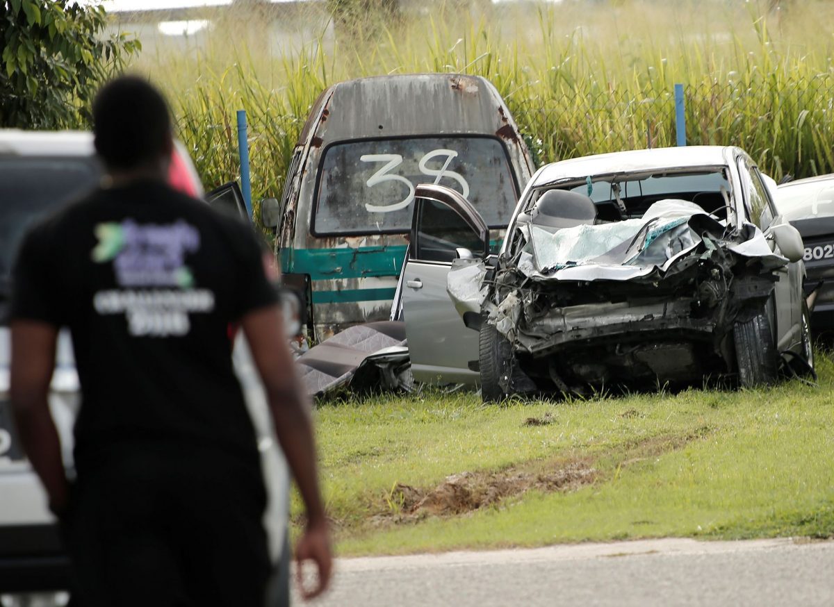 ABOVE: A police officer looks at the wrecked Nissan Tiida at the back of the Cunupia Police station yesterday morning.