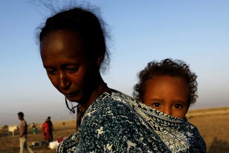 An Ethiopian woman who fled the ongoing fighting in Tigray region, carries her child near the Setit river on the Sudan-Ethiopia border in Hamdayet village in eastern Kassala state, Sudan November 22, 2020. REUTERS/Mohamed Nureldin Abdallah