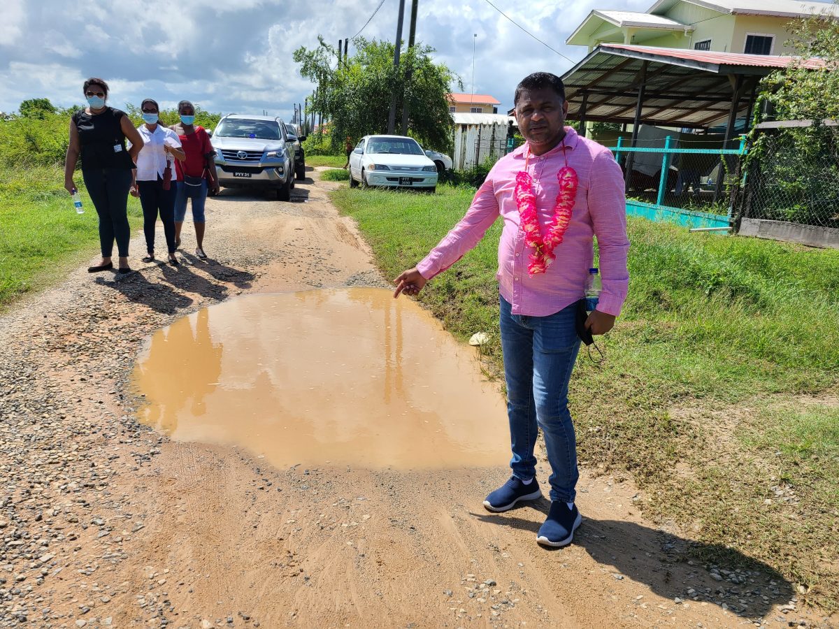 Minister in the Ministry of Public Works, Deodat Indar standing next to a pothole in the area. (Ministry of Public Works photo)