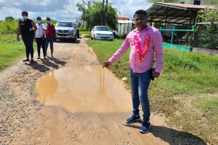 Minister in the Ministry of Public Works, Deodat Indar standing next to a pothole in the area. (Ministry of Public Works photo)