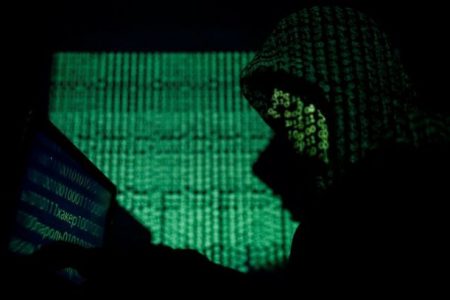 FILE PHOTO: A hooded man holds a laptop computer as cyber code is projected on him in this illustration picture taken on May 13, 2017. REUTERS/Kacper Pempel