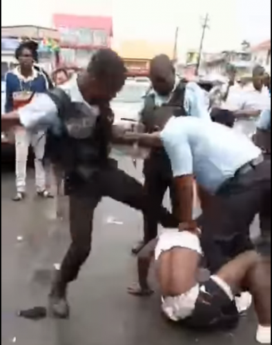 A member of the Guyana Police Force kicks a suspect in the head while two other officers restrain him