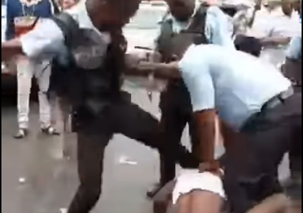 A member of the Guyana Police Force kicks a suspect in the head while two other officers restrain him