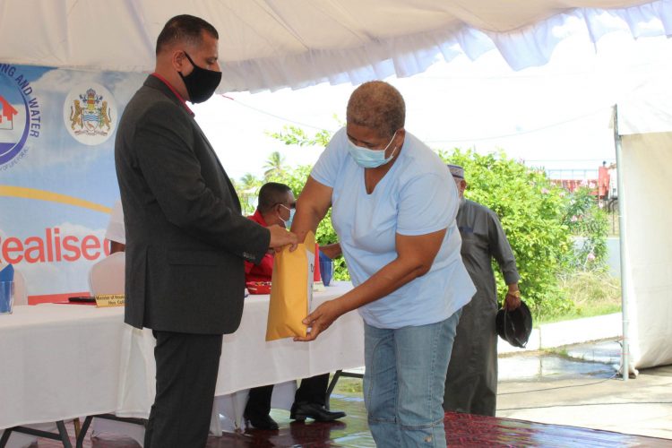 Minister Collin Croal (left) assisting one of the recipients to pick a number for her lot