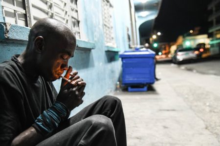 Lionel Johnson, 47, lights a cigarette while sitting outside the Kingston and St Andrew Municipal Corporation temporary night shelter on Church Street. Deported from New York almost two decades ago, Johnson said he has no relatives here in Jamaica. He said he was shocked to hear about the brutal attacks on the homeless that left four dead and two injured.

