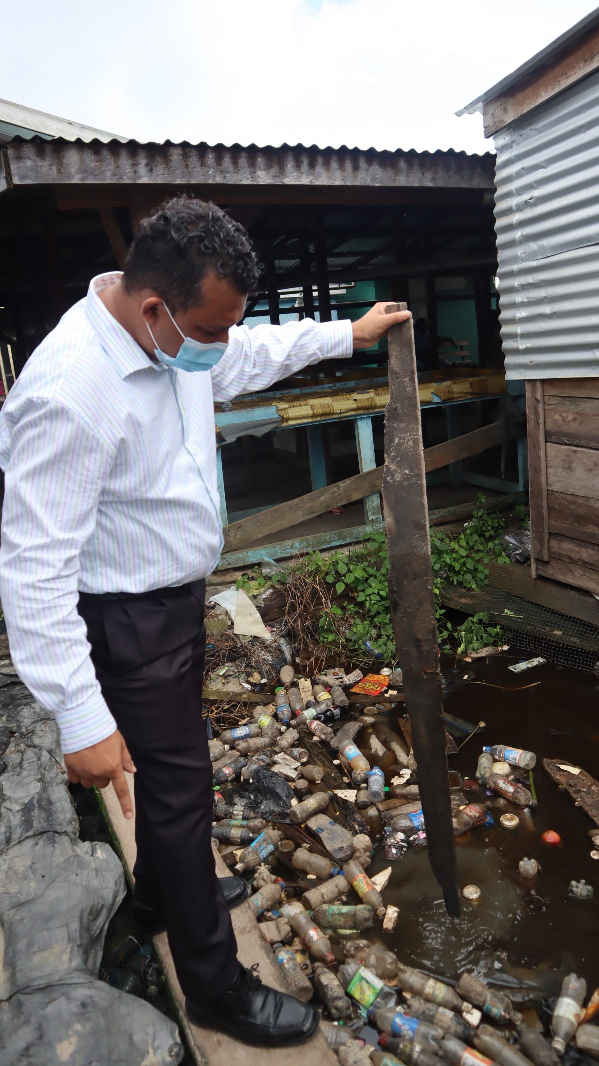 Regional Executive Officer Devanand Ramdatt testing the flood depth amid debris (Ministry of Agriculture photo)