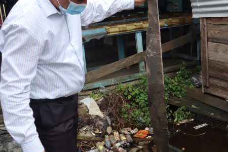 Regional Executive Officer Devanand Ramdatt testing the flood depth amid debris (Ministry of Agriculture photo)