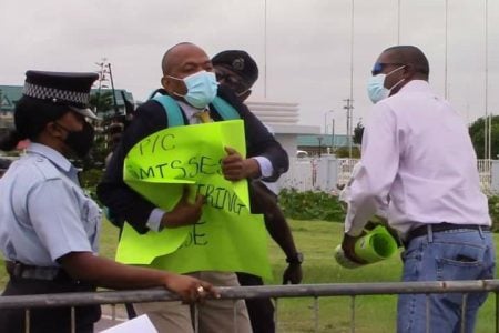 Opposition Parliamentarian Sherod Duncan (centre) being restrained by a member of the Guyana Police Force as he attempted to enter the Arthur Chung Convention Centre with a placard. His colleague former Ministers of Public Infrastructure David Patterson (right) attempted to intercede on his behalf. (Photo credit Joseph Allen) 