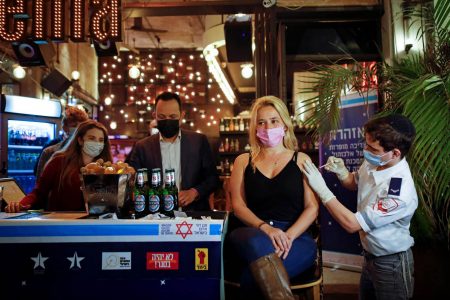 A woman receives a vaccination against COVID-19 as part of a Tel Aviv municipality initiative offering free drinks to residents getting a shot. (REUTERS/Corinna Kern photo)