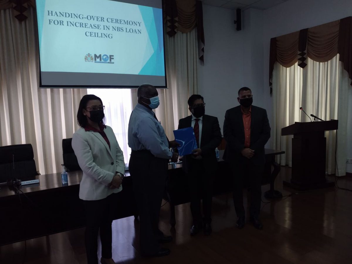 Minister of Finance Dr Ashni Singh (second from right) hands over the instrument to allow for an increase in the loans value from $12M to $15M to NBS Chairman Floyd Mc Donald. They are flanked by Ministers of Housing and Water Collin Croal (right) and Susan Rodrigues. 