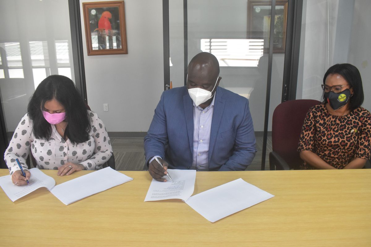 Permanent Secretary of the Ministry and Tourism, Industry and Commerce, Sharon Roopchand-Edwards (left), and Justin Nedd of Arrowhead Communications signing the MoU, while Minister of Tourism, Industry and Commerce, Oneidge Walrond observes