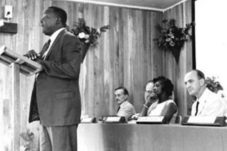 Harold Davis, as Education and Training Officer delivering the keynote speech at the Port Mourant Apprentice Training School First Graduation in 1962. Sitting L to R: R. Fletcher (first Principal), F.H. Thomasson, Chief Personnel Officer (partly hidden), Winifred Gaskin, Minister of Education, E.S. Readwin, Chairman, BSE Ltd
