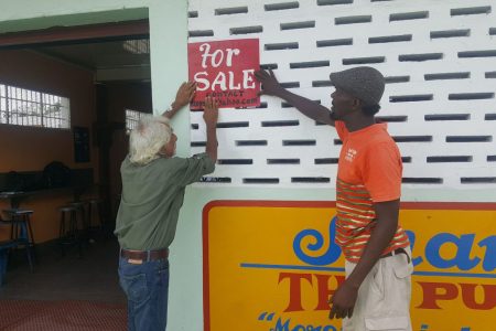 Deodatt Persaud (left) erecting a ‘For Sale’ sign on the building  in 2019.