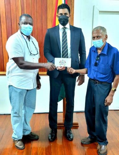 Minister of Sport, Charles Ramson Jr. presents the sponsorship cheque to President of the GCF, Linden Dowridge (left) in the presence of legendary cycling events organizer, Hassan Mohamed.