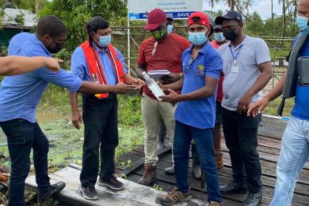 GWI CEO Shaik Baksh (second from left) and others examining a water sample on the island (GWI photo)