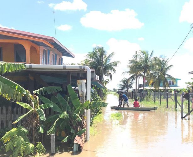 Villagers in Wash Clothes, Mahaicony using a boat to traverse an access road covered by floodwater