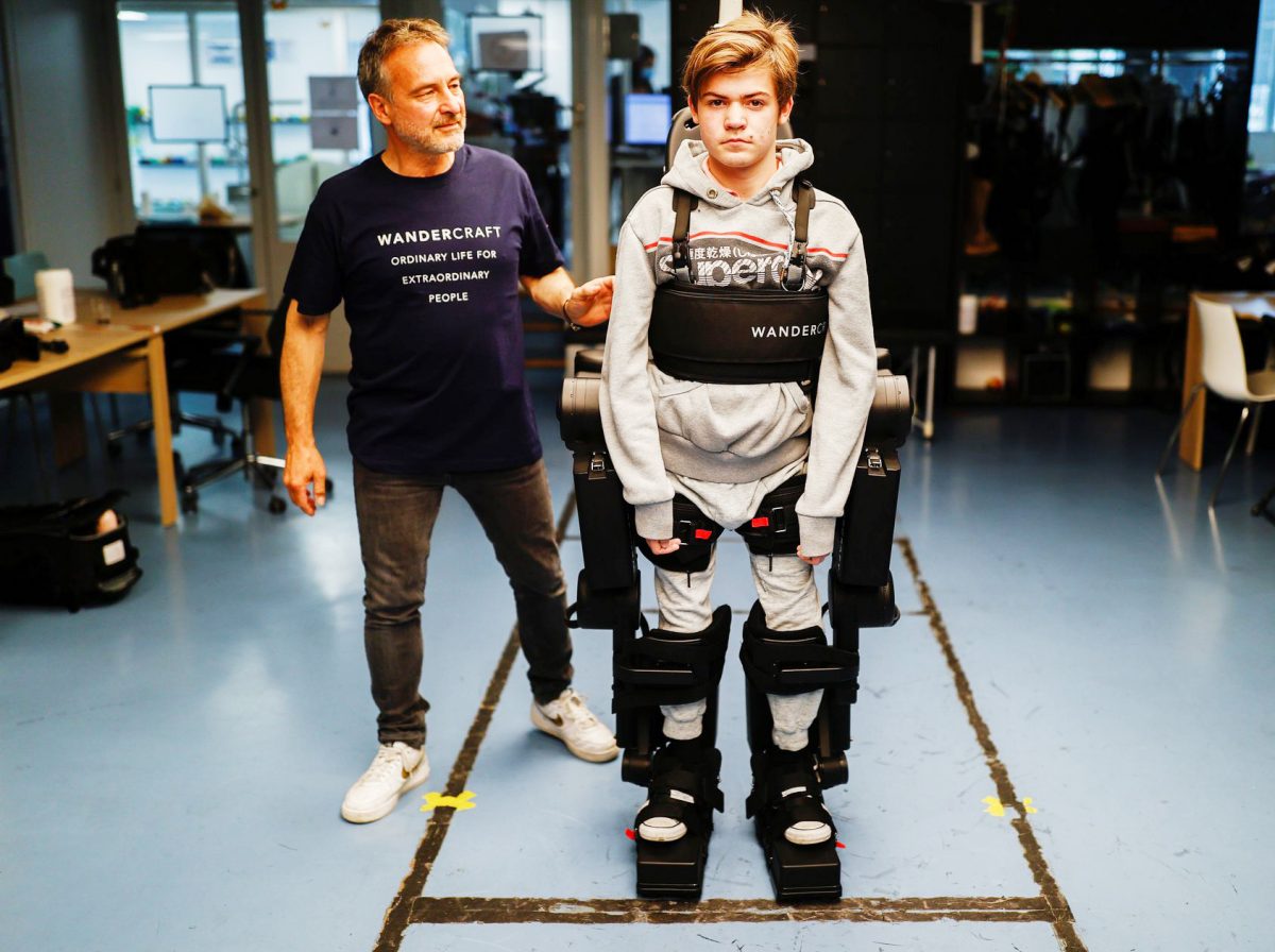 Jean-Louis Constanza, Chief Business and Clinical Officer at French company Wandercraft helps his 16-year-old son Oscar using a robot exoskeleton at the company headquarters in Paris, France July 9, 2021. Picture taken July 9, 2021. (REUTERS/Christian Hartmann photo) 