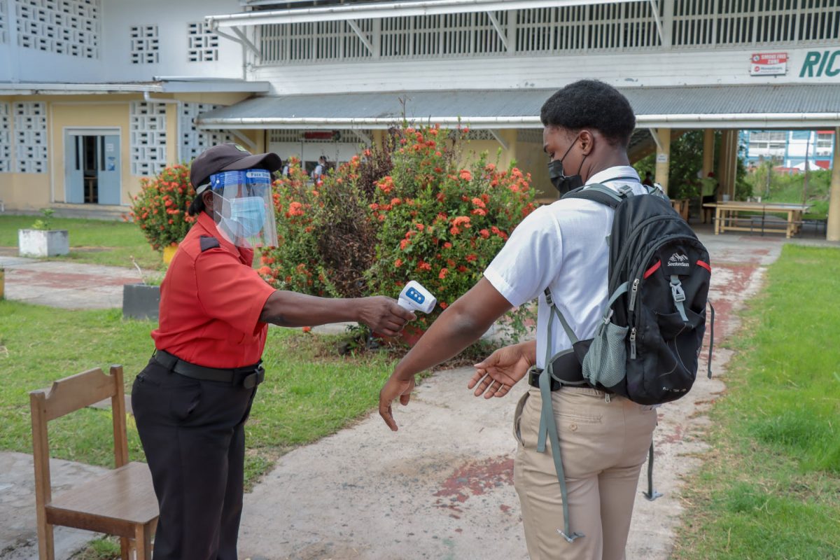 A guard checks the temperature of a student at the Richard Ishmael Secondary. The check are part of COVID-19 safety measures instituted at schools for the holding of classes and examinations (Ministry of Education photo) 