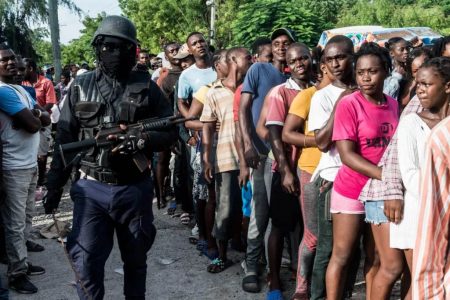 A police officer watches as earthquake victims line up during the distribution of food and water at the “4 Chemins” crossroads in Les Cayes, Haiti. (Photo: Getty Images)