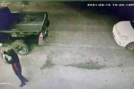 A screenshot from one of the surveillance videos showing one of the suspects (at lower left) firing at one side of the pick-up, with the getaway car parked at right
