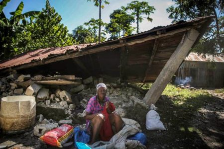 A woman sits in front of a destroyed house after the earthquake in Camp-Perrin, Les Cayes, Haiti, Sunday, Aug. 15, 2021. The death toll from the magnitude 7.2 earthquake in Haiti soared on Sunday as rescuers raced to find survivors amid the rubble ahead of a potential deluge from an approaching tropical storm. (AP Photo/Joseph Odelyn)