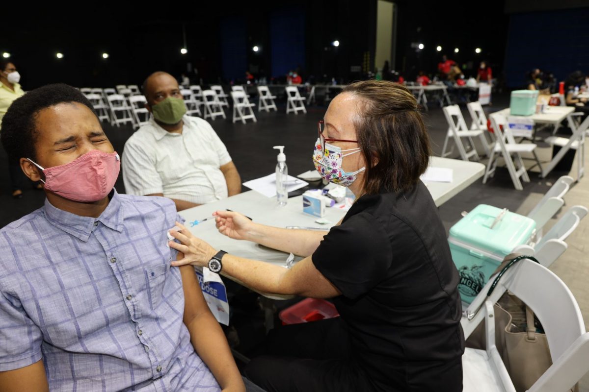 Paediatrician Dr Catherine Charles administers the Pfizer vaccine to 15-year-old Javier Thompson at the National Academy for the Performing Arts in Port-of-Spain yesterday. Seated at the back is Edsel Thompson, Javier’s father.
