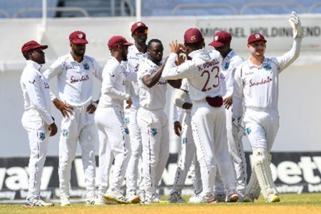 West Indies players gather around Kemar Roach to celebrate the day’s first wicket of Abid Ali yesterday.