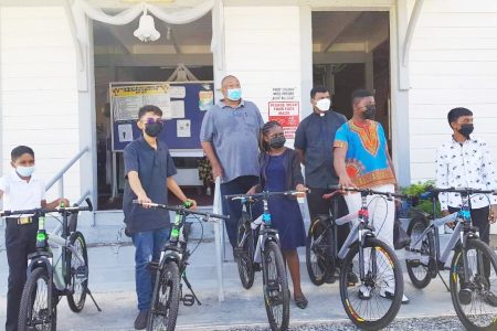 RHTYSC Secretary Hilbert Foster (third from left) and Parish Priest Ramesh Vanan (to Foster’s right) pose with the five youths and the bicycles.