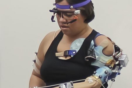 A participant at Cleveland Clinic with her advanced prosthetic arm that feels grip movement sensation, touch on the fingertips, and is controlled intuitively by thinking. She is wearing reflective markers on her arms and body that help a computer see her movements in a 3D environment. Her glasses allow a computer to see exactly what her eyes are looking at in the space around her. (Cleveland Clinic photo)