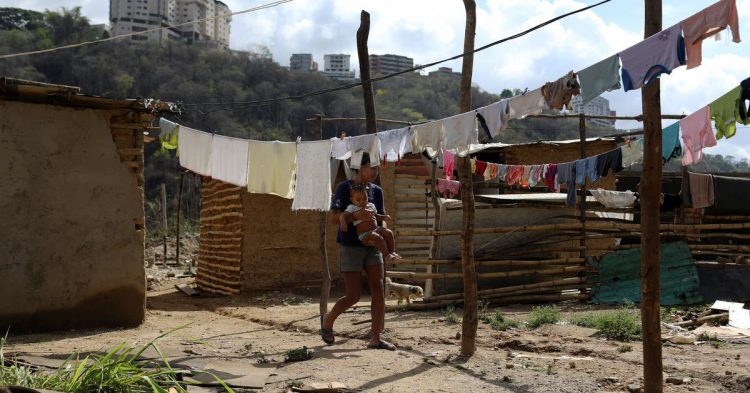 A woman walks across hanged clothes on a vacant lot where families are settling since they cannot afford to pay rent anymore, in the municipality of Sucre, near Caracas, Venezuela June 12, 2020. REUTERS/Manaure Quintero