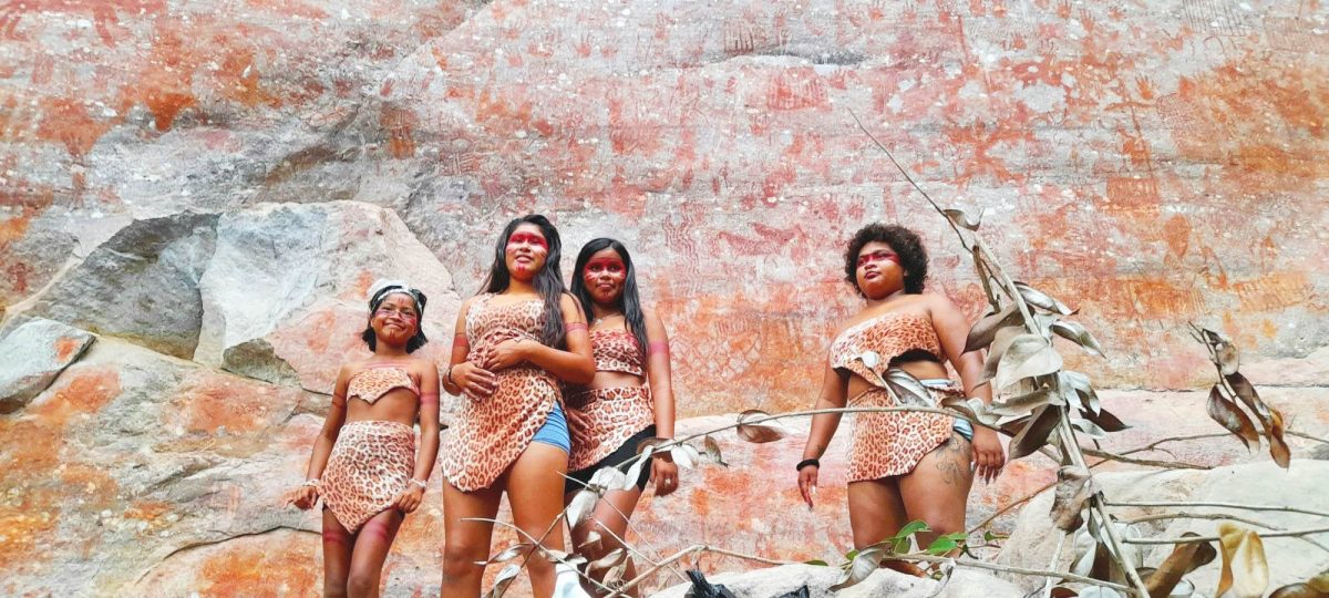 Arrayed in their costumes and baring painted faces, the young women of Ibaimadai proudly stand beside the paint rock
