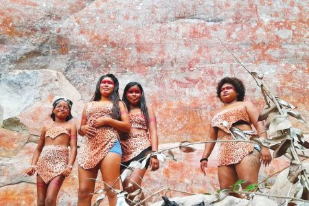 Arrayed in their costumes and baring painted faces, the young women of Ibaimadai proudly stand beside the paint rock