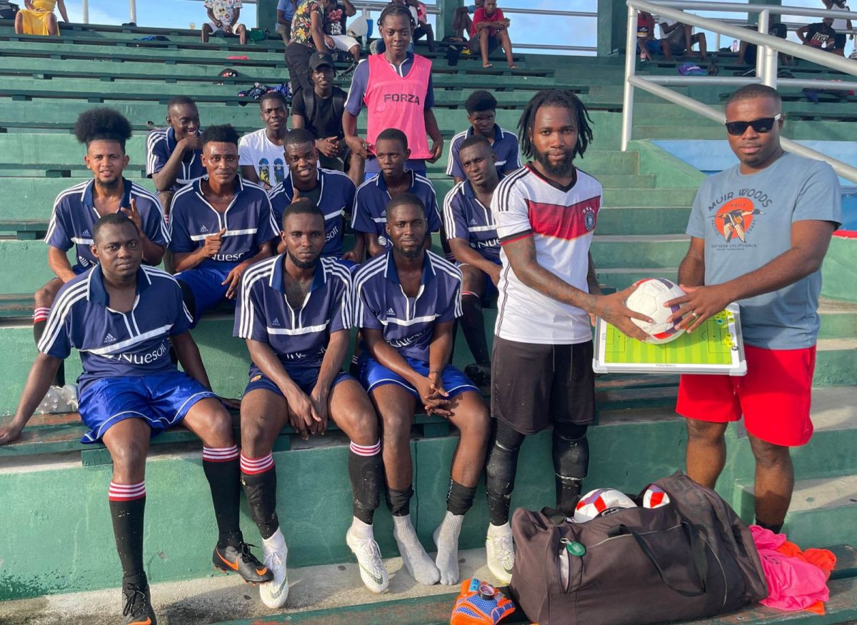 Pouderoyen FC captain and goalkeeper Sherwin Wills, receiving the donation from former player Anton Peterson in the presence of several of his teammates at the National Track and Field Centre, Leonora
