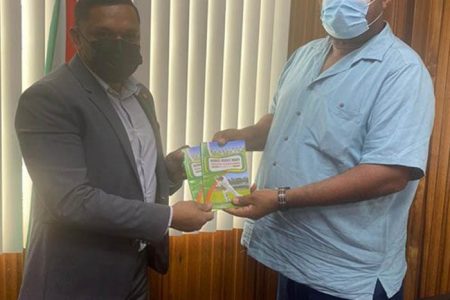BCB President Hilbert Foster (right) hands over copies of the board historic coaching manual to BCB Patron Minister Vickram Bharrat.