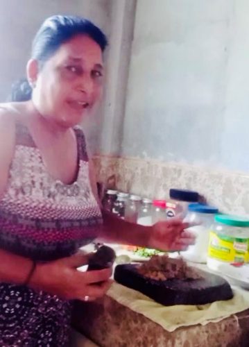 A screenshot of Elaine in her kitchen, demonstrating how to make coconut choka during a live video