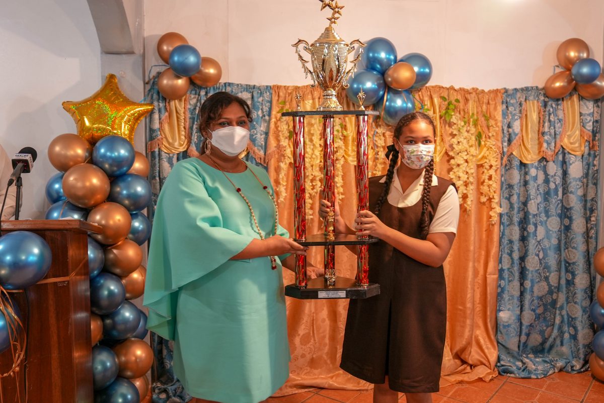 Minister of Education Priya Manickchand handing over the trophy to the region’s top performer Gizelle Nicholson from Leonora Primary who achieved 520 marks and was awarded a place at Queen’s College. (Ministry of Education photo) 