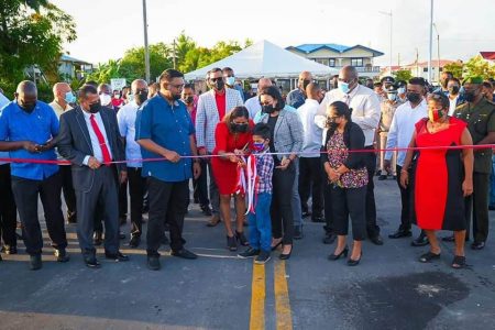 A young resident of Diamond, East Bank Demerara cuts the ribbon marking the opening of the road in the presence of President Irfaan Ali, Ministers of Housing and Water Collin Croal and Susan Rodrigues and Minister of Home Affairs Robeson Benn among others. (Office of the President photo)