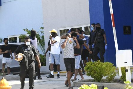 DETAINED: Some of the persons who were detained, after being found on a yacht early yesterday morning, cover their faces as they are escorted out of the Carenage Police Station for further enquiries yesterday.
—Photo: JERMAINE CRUICKSHANK
