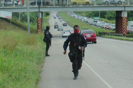 Police officers on the Sir Solomon Hochoy Highway, Couva after the shootout between police and bandits, yesterday.